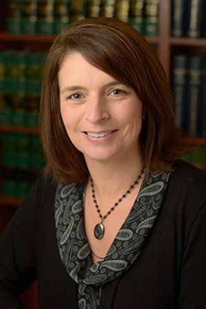 A woman wearing a necklace and a black shirt is smiling in front of a bookshelf.