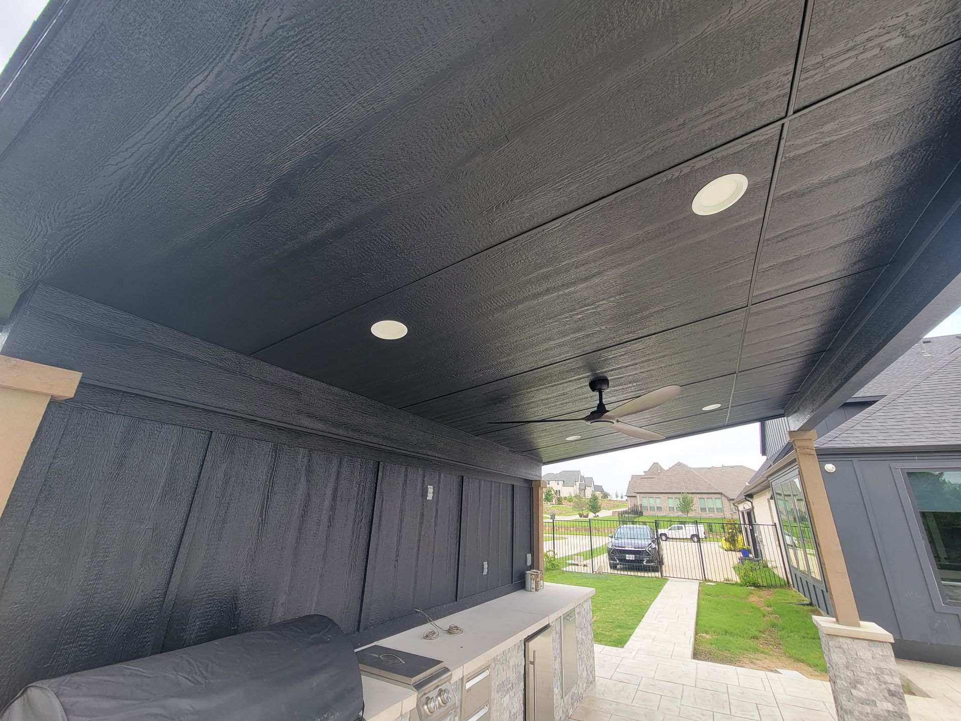 Covered outdoor patio with black ceiling, recessed lights, storage cabinets, and a walkway to a driveway.
