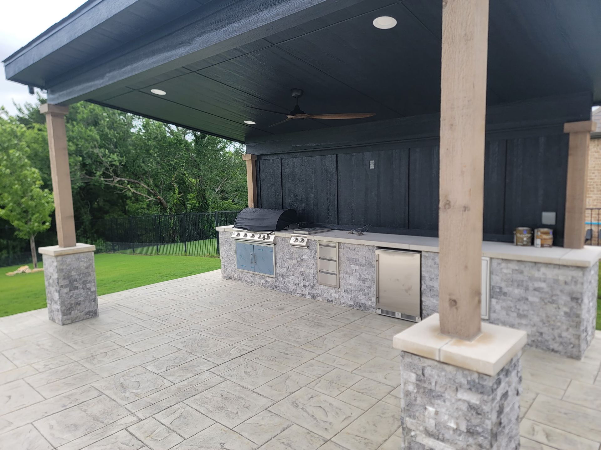 Outdoor covered grill area with stone counters and a paved patio under a roof