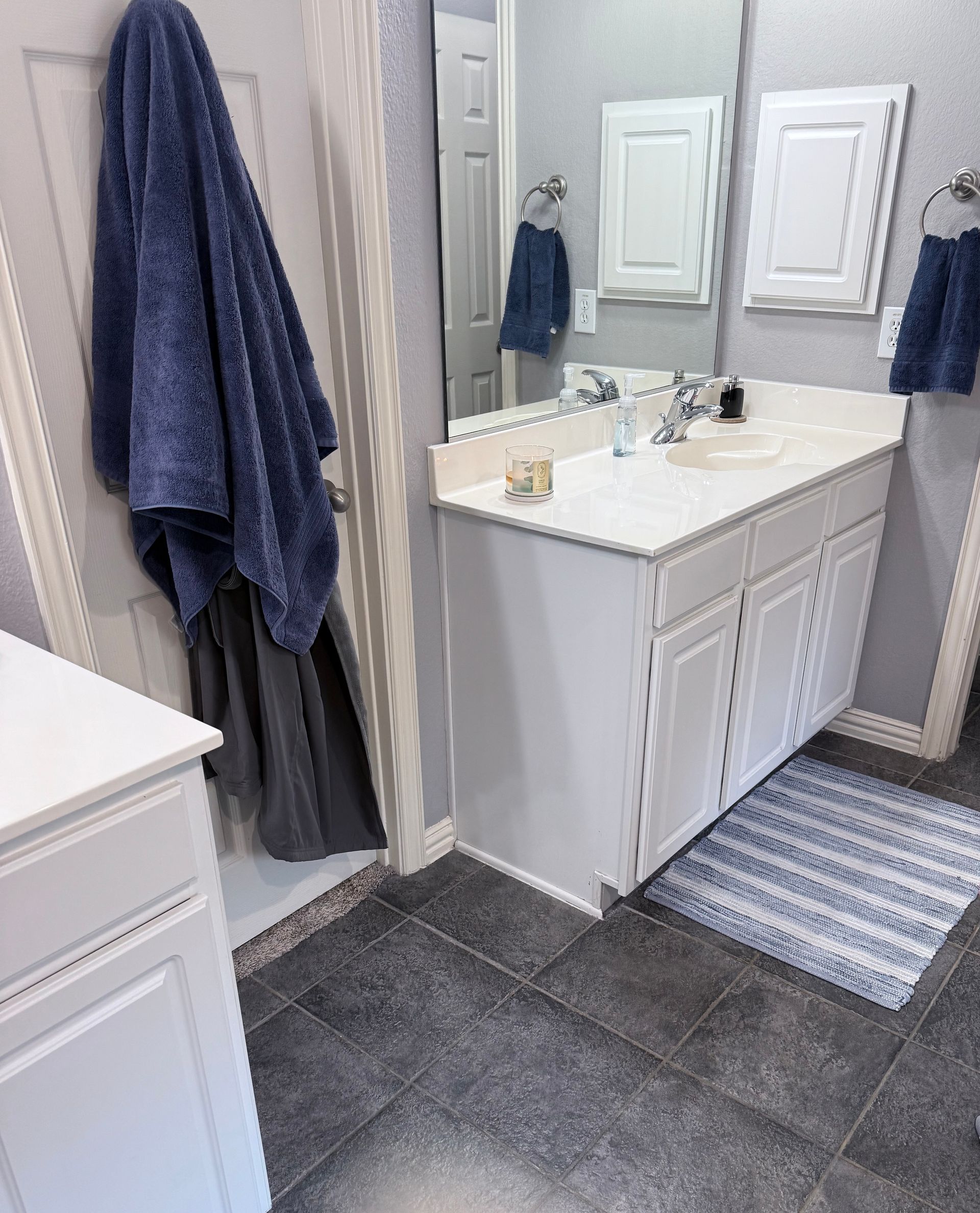 Small bathroom with white vanity, mirror, towels, and dark gray tile floor.