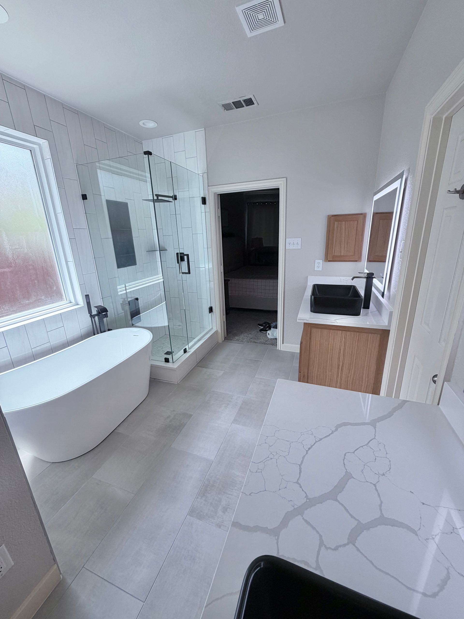 Bright modern bathroom with freestanding tub, glass shower, vanity, and marble-patterned floor tiles