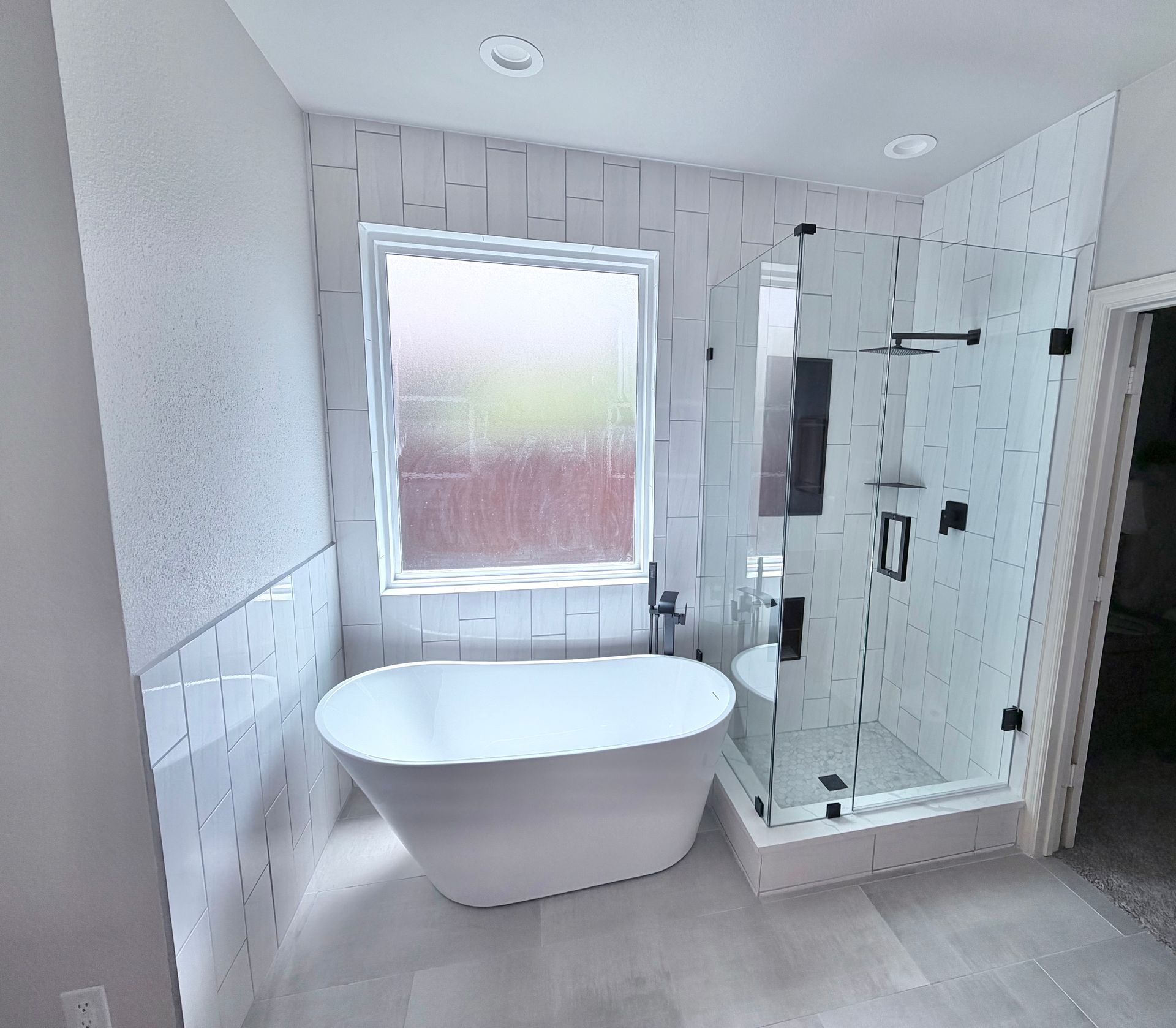 Modern bathroom with freestanding tub, glass shower, frosted window, and white tiled walls