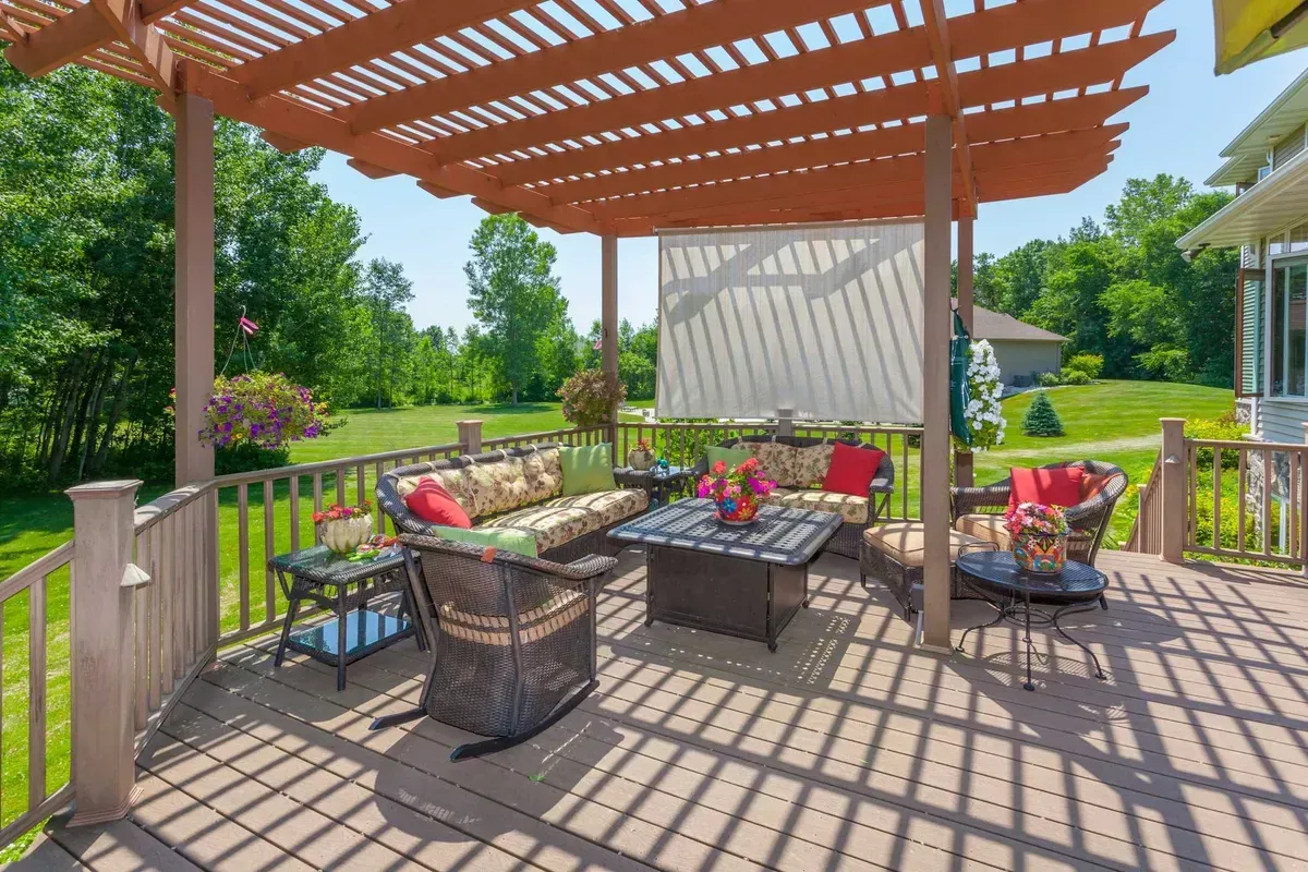Wooden deck with outdoor seating under a pergola; includes a fire pit and a screen.