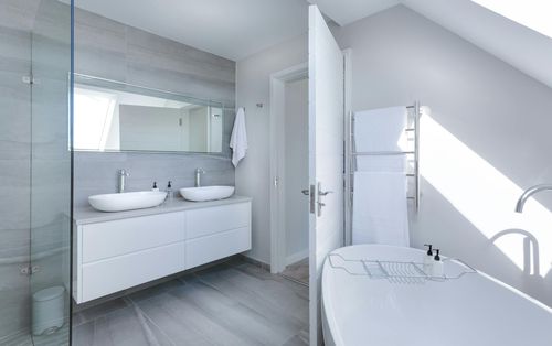 Modern white bathroom with double sinks, tub, and glass shower.