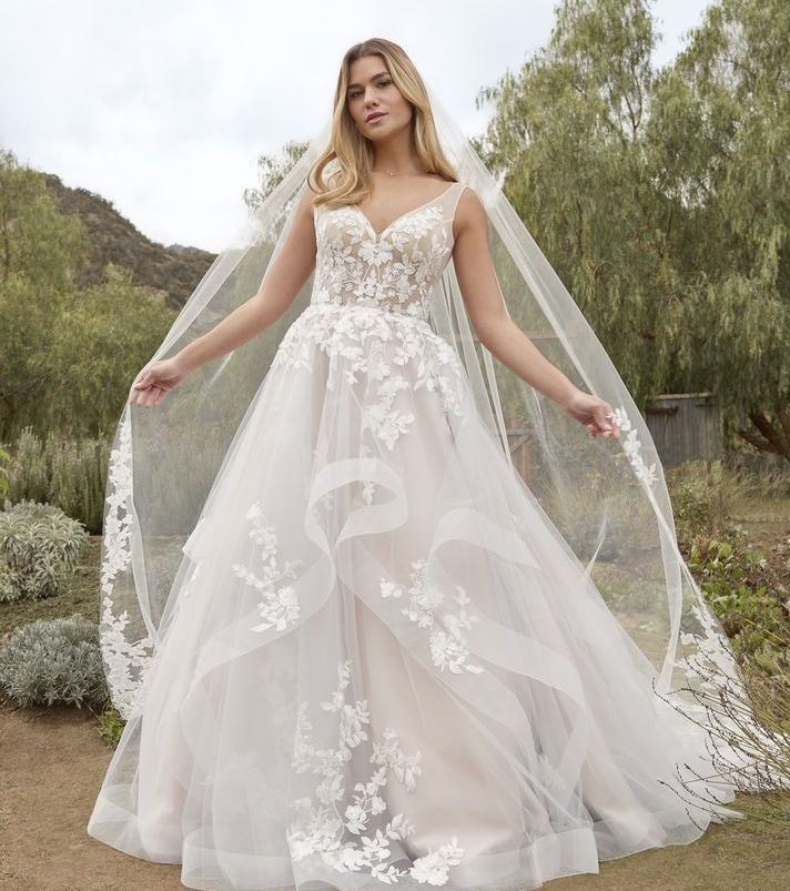 A woman in a white wedding dress is standing in front of a white wall.