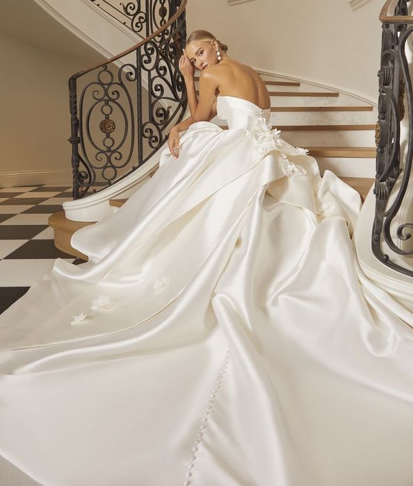A woman in a wedding dress is standing in front of a building next to a car.