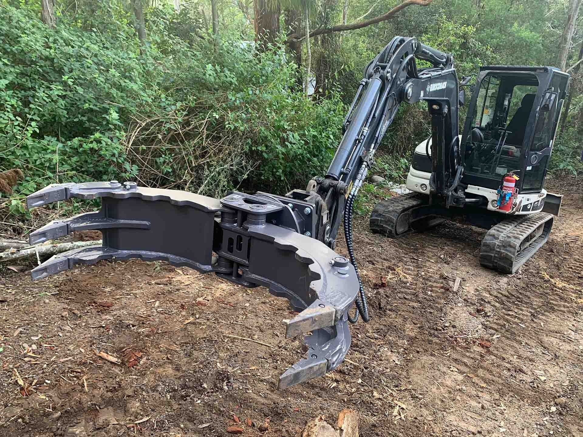 Black Excavator With Grapple Attachment in a Wooded Area — All Tree Solutions In North Avoca, NSW