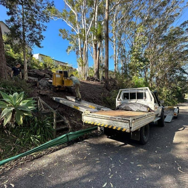 A White Flatbed Truck Loads a Yellow Mini-excavator — All Tree Solutions In HOLGATE, NSW