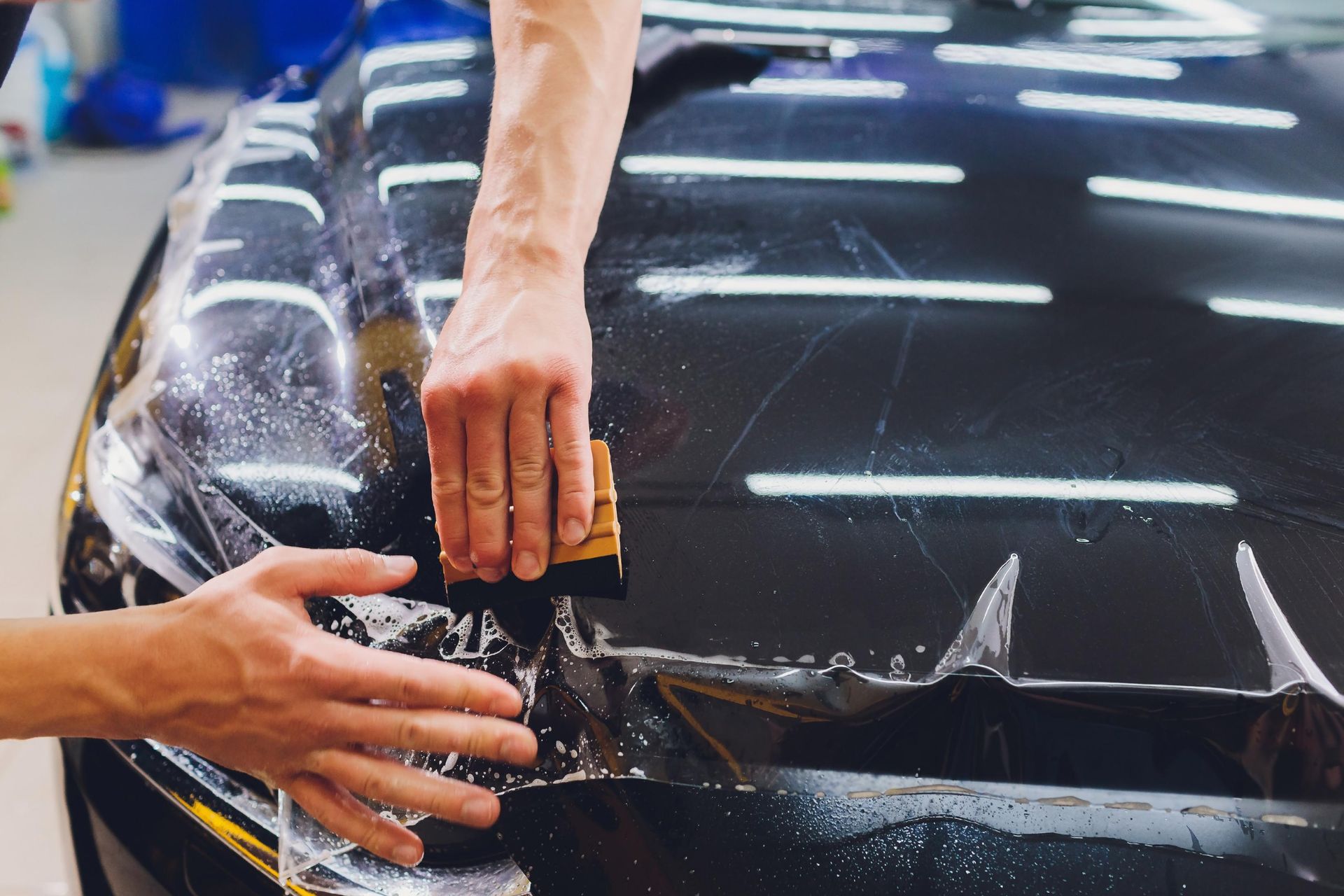 Person applying protective film to a black car hood, using a squeegee.