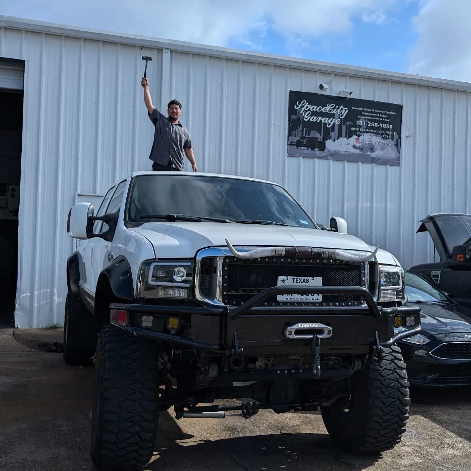 Mechanic Standing On Lifted Truck Outside Shop | Full-Service Auto Repair