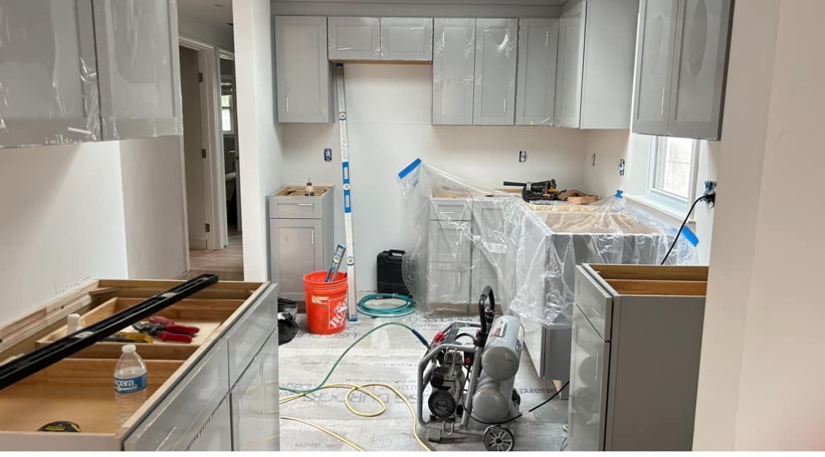A kitchen under construction with white cabinets and a bucket on the floor.