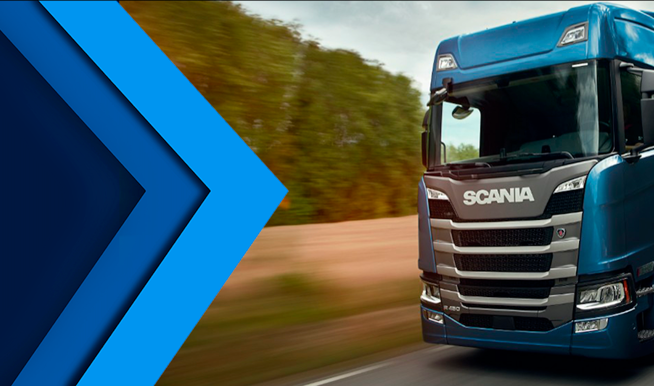 Um caminhão Scania azul trafegando em uma estrada ao lado de um campo, com um chamativo desenho em forma de V azul à esquerda.