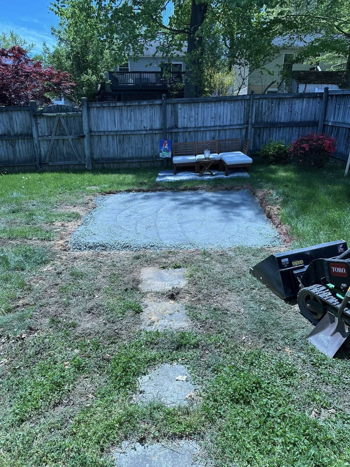 Gravel patio being built in a backyard, next to a lawn with a mini-excavator.