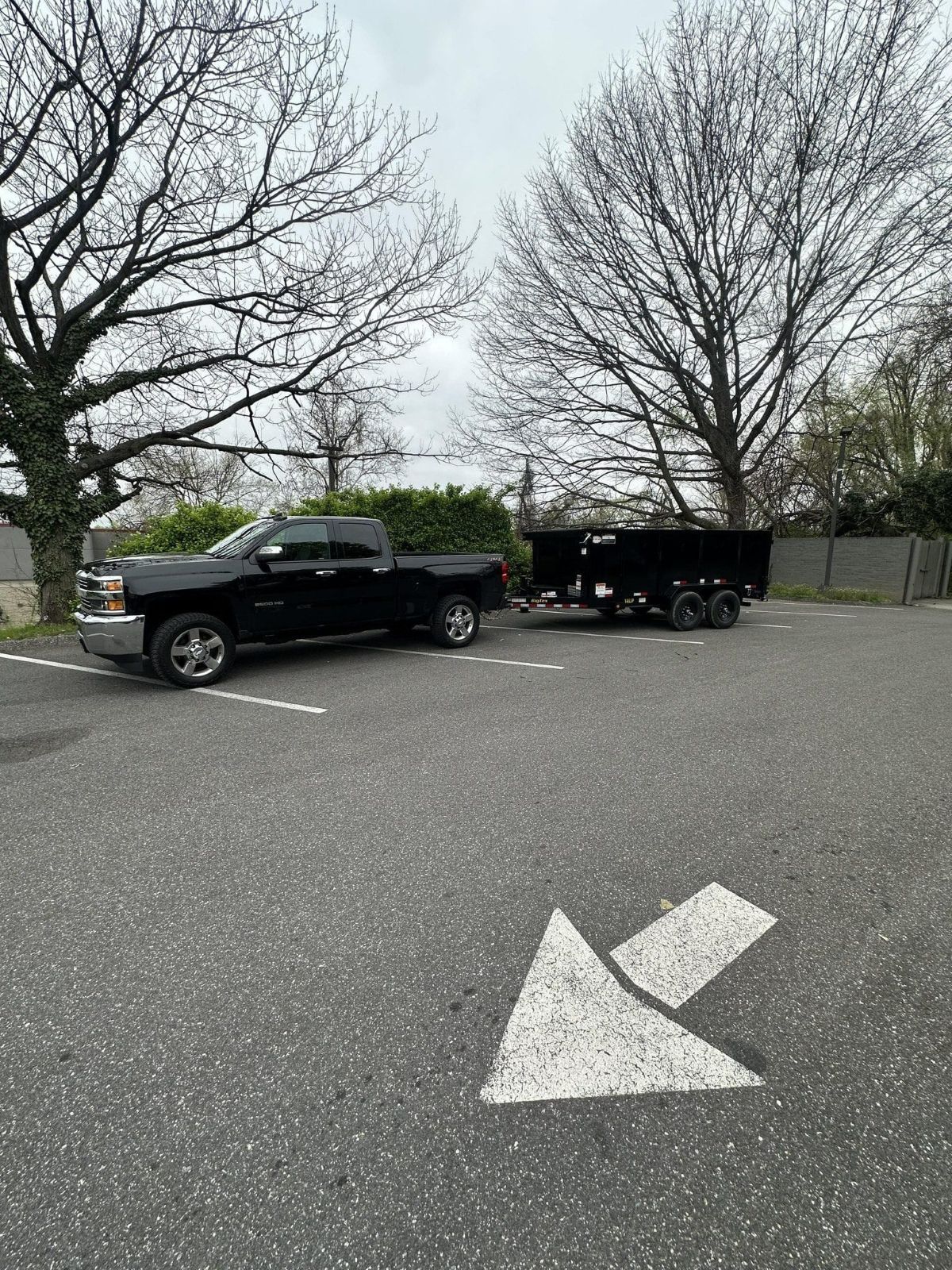 Black truck towing a black trailer in a parking lot with a painted arrow.