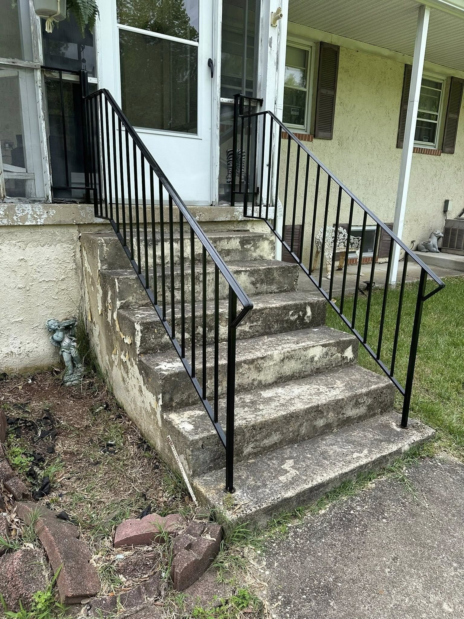 Concrete steps leading to a white door with black iron railings.