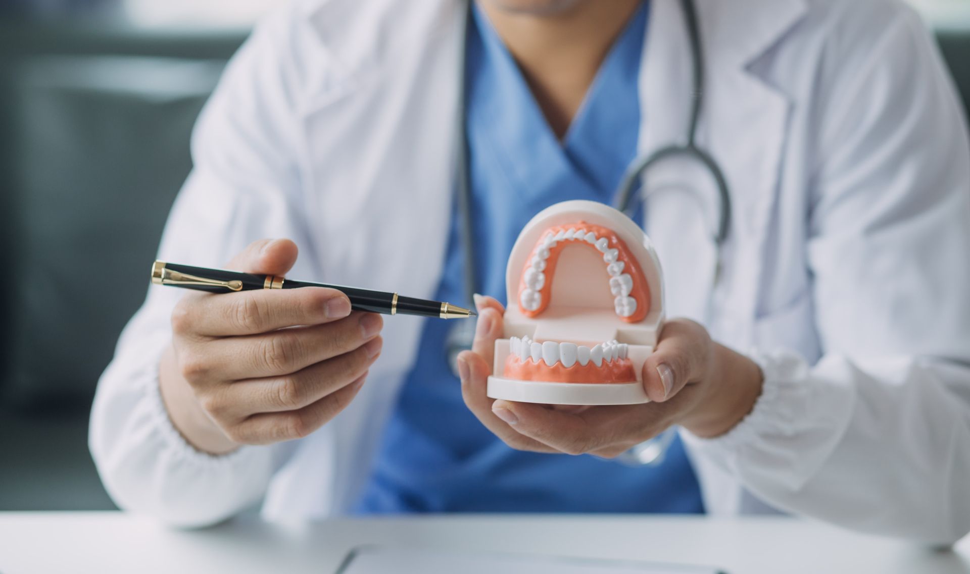 Dentist in blue scrubs holding a dental model and pointing with a pen