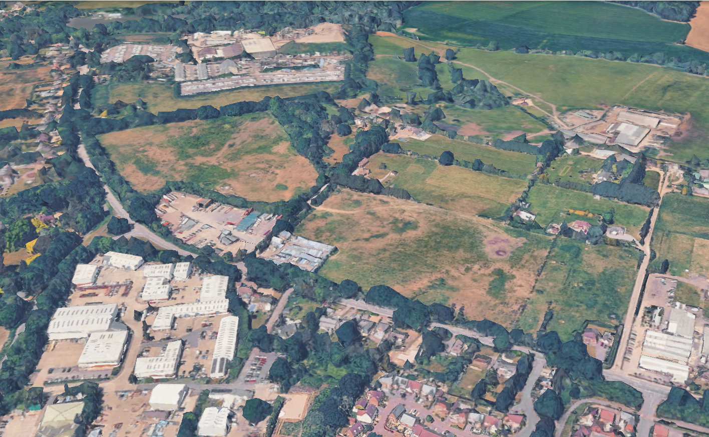 An aerial view of a semi-rural landscape with industrial buildings, residential blocks, and green fields.