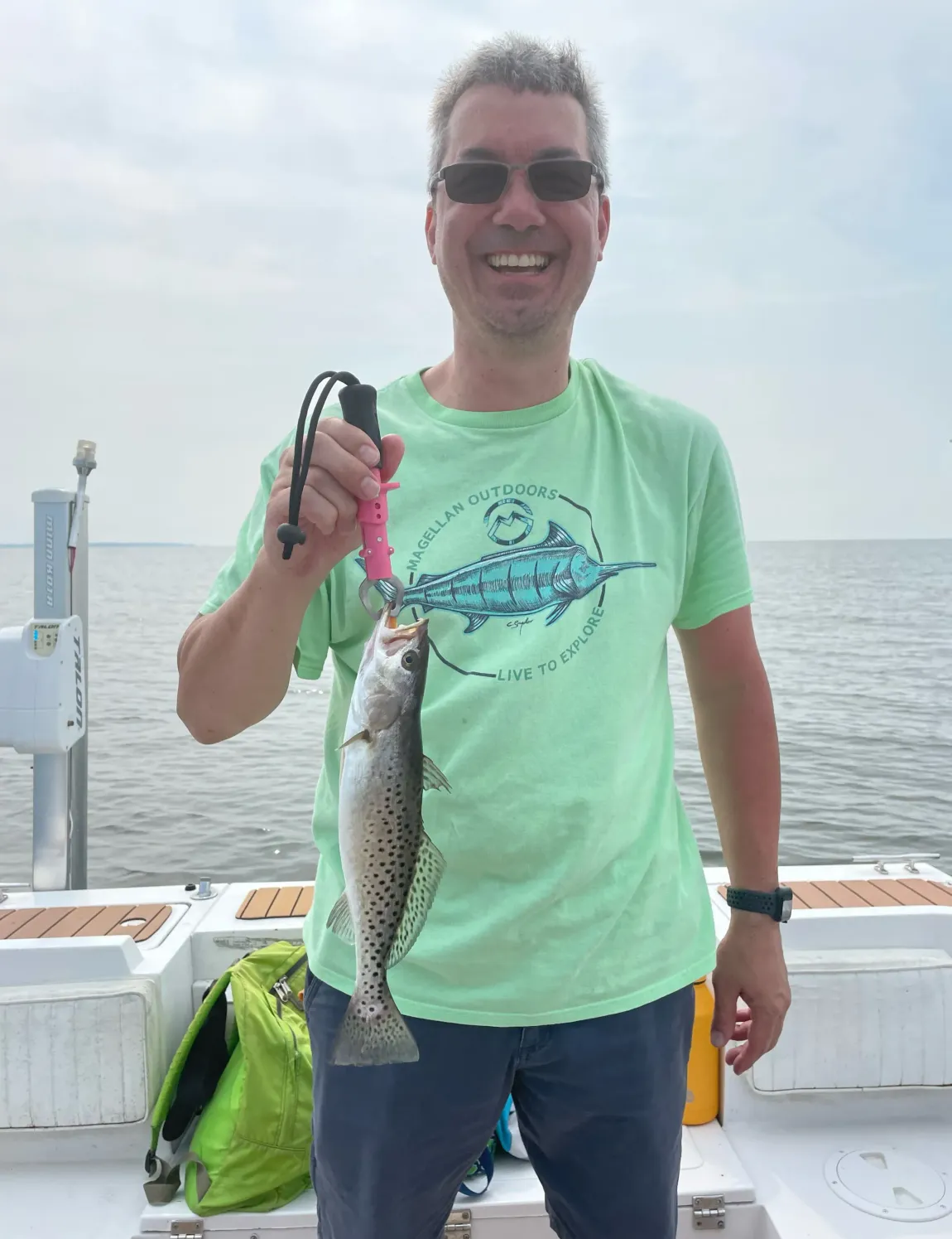 A man in a green shirt is holding a fish on a boat.