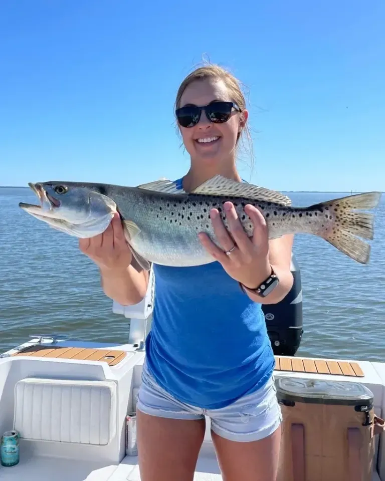 A woman is holding a large fish in her hands on a boat.