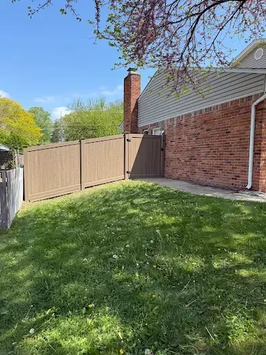A fence surrounds a lush green yard in front of a brick house.