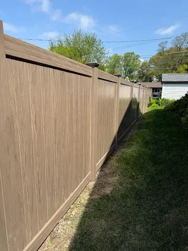 A rich brown vinyl fence encloses a vibrant, lush green yard.