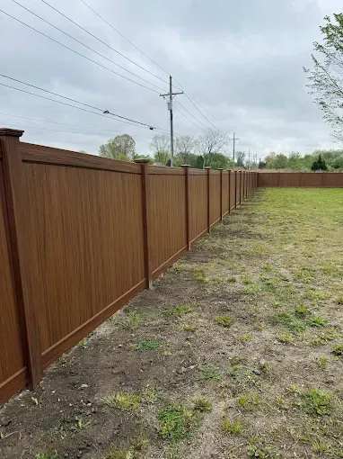 A vinyl fence is sitting in the middle of a grassy field.
