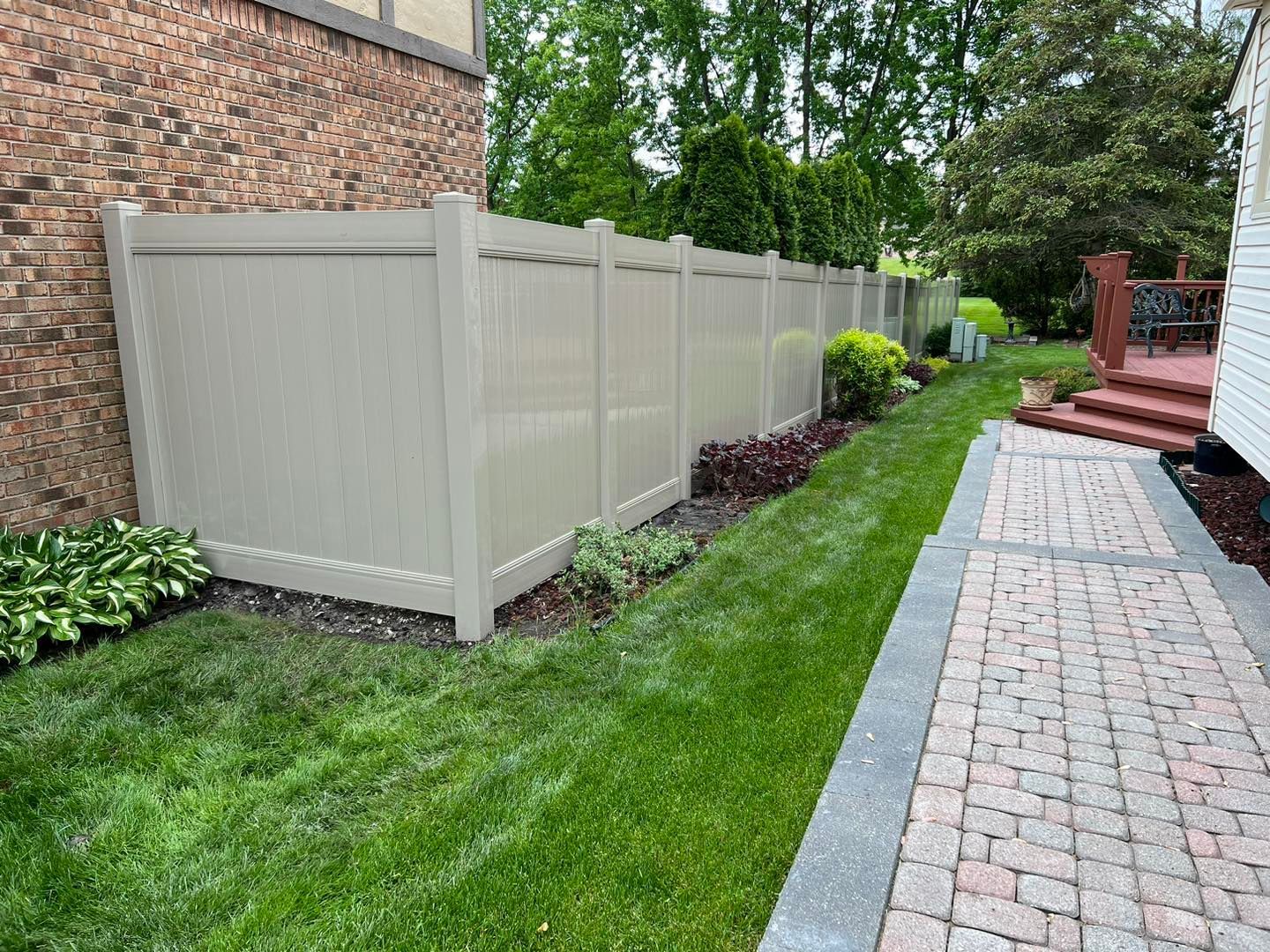 a white fence surrounds a lush green yard next to a brick walkway.