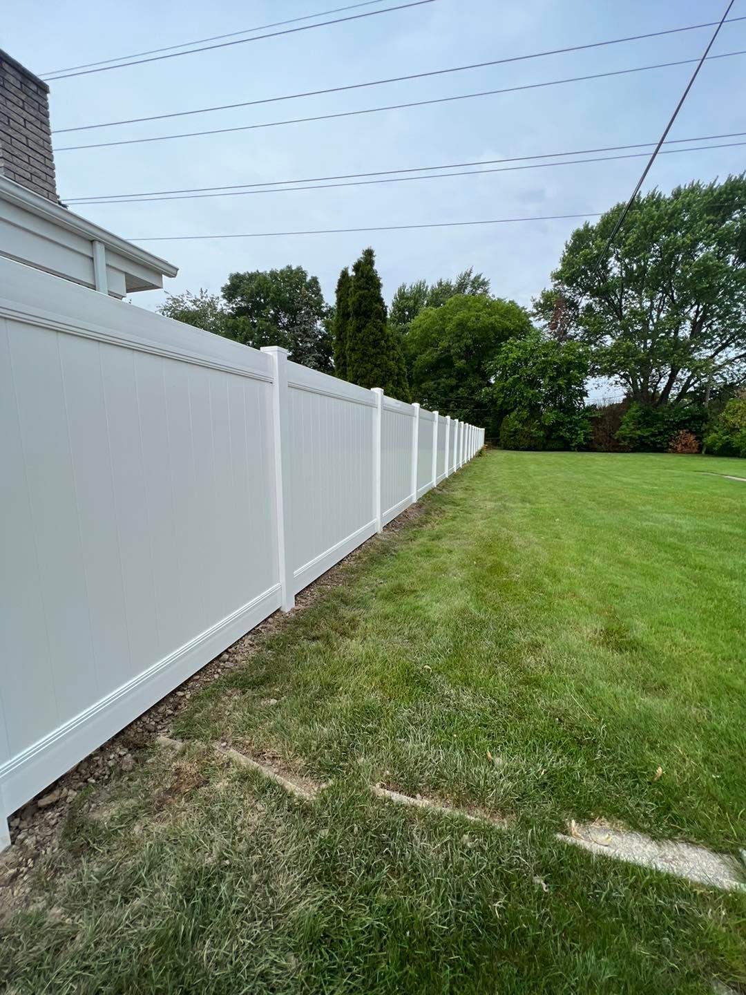 a white fence surrounds a lush green yard surrounded by trees.