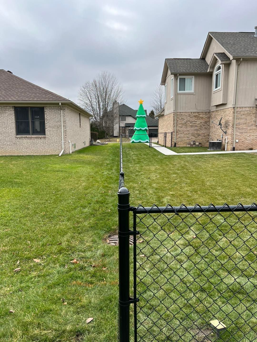 a chain link fence surrounds a brick house with an inflatable Christmas tree in the front.