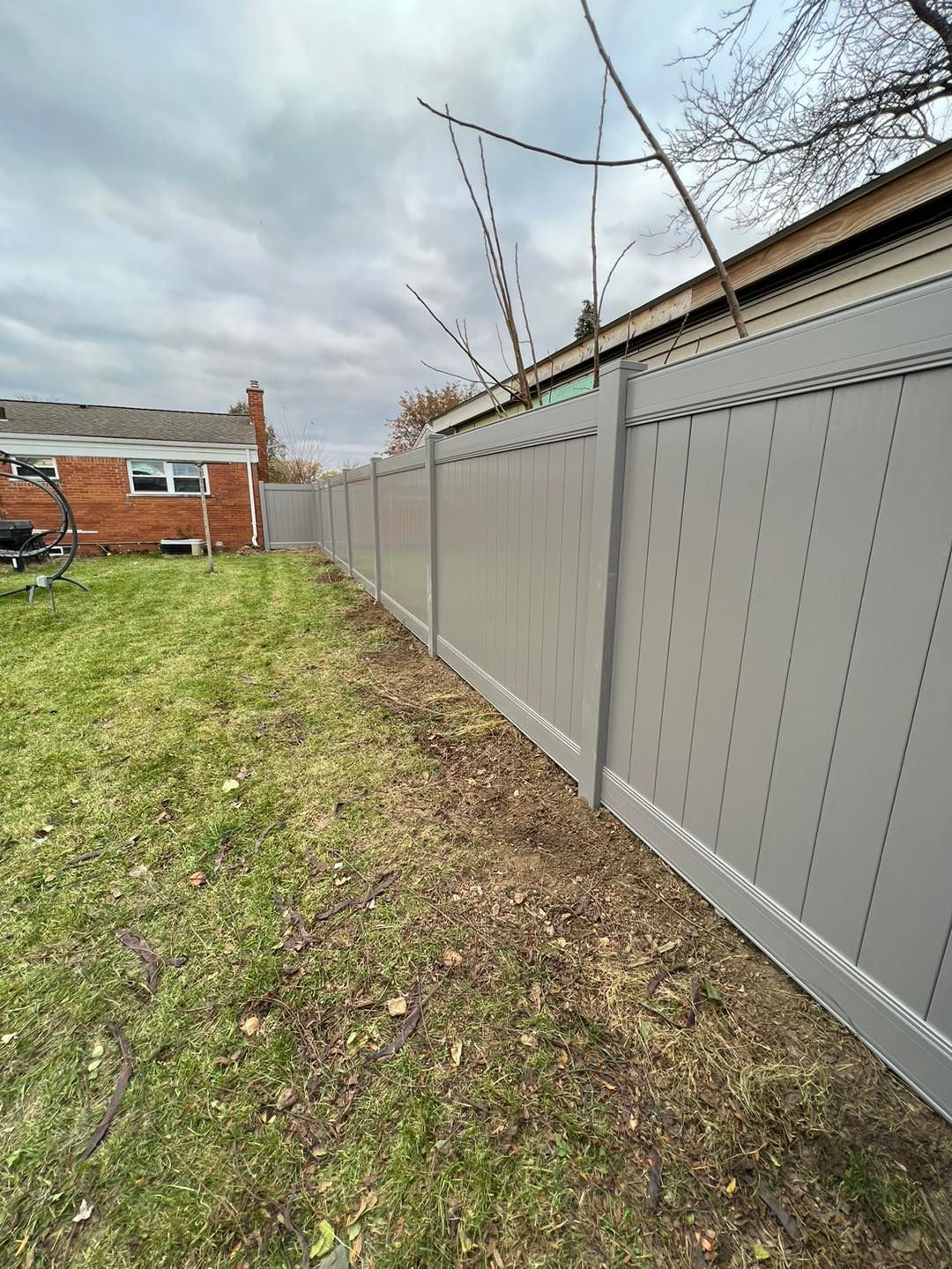a gray fence surrounds a backyard with a brick house in the background.