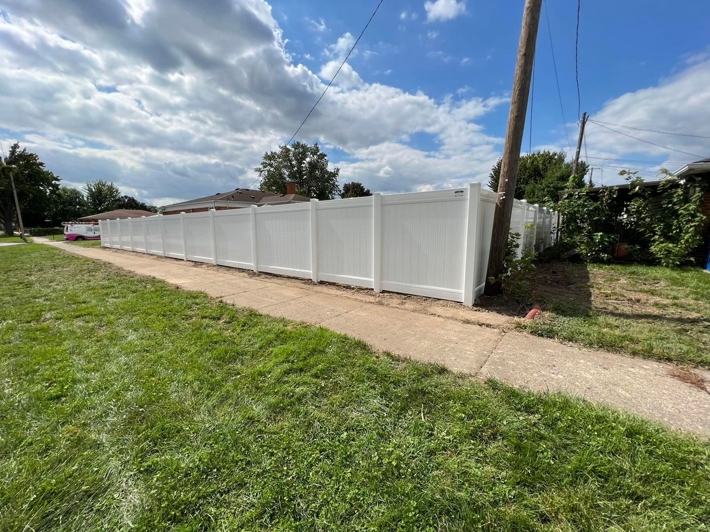 a white fence along a sidewalk in front of a house.