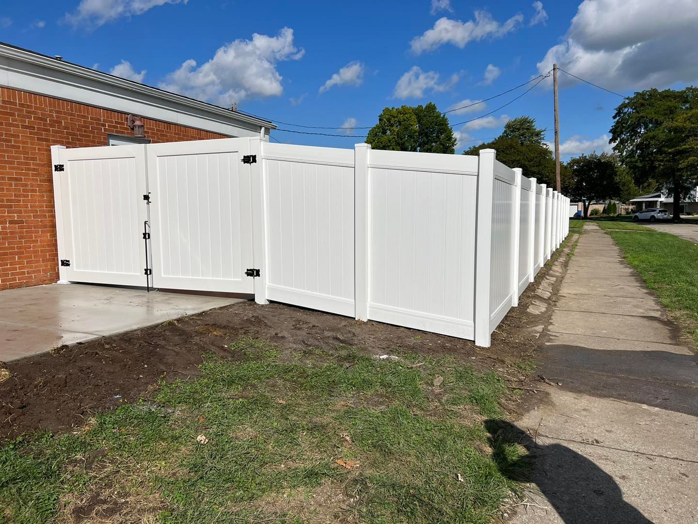 a white fence along a sidewalk next to a brick house.