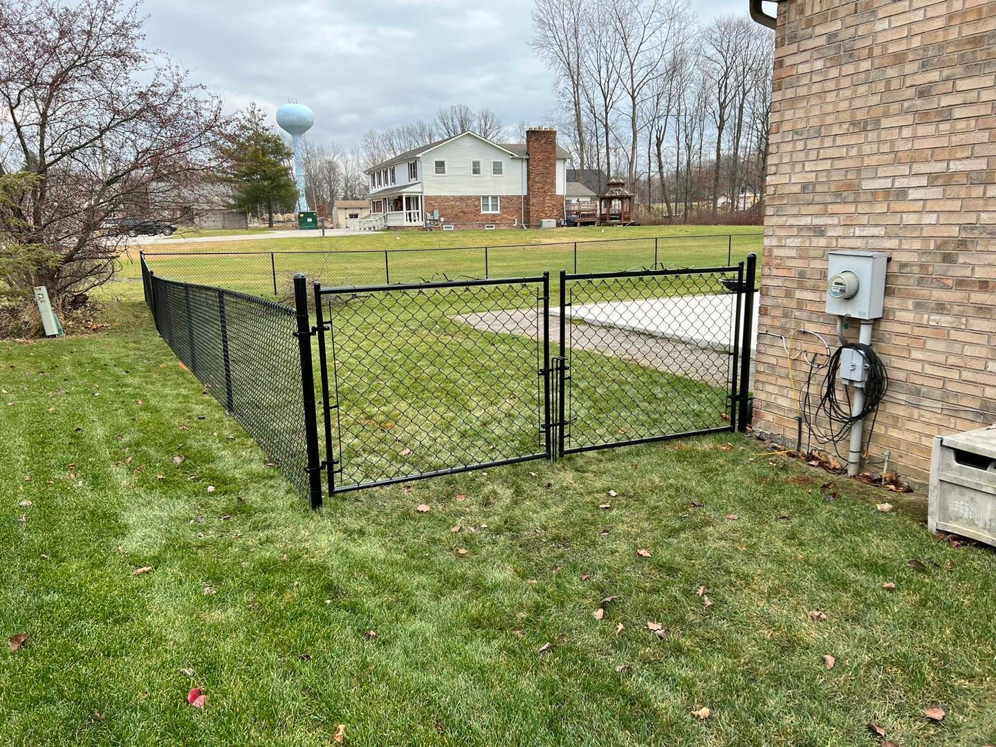 a black chain link fence surrounds a brick house.