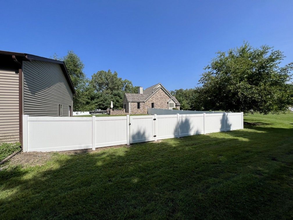A white fence surrounds a yard with a house in the background