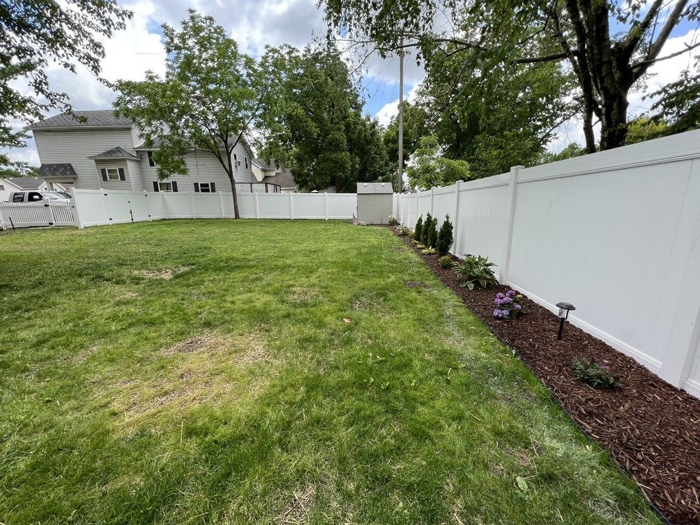 A large yard with a white fence and a house in the background.