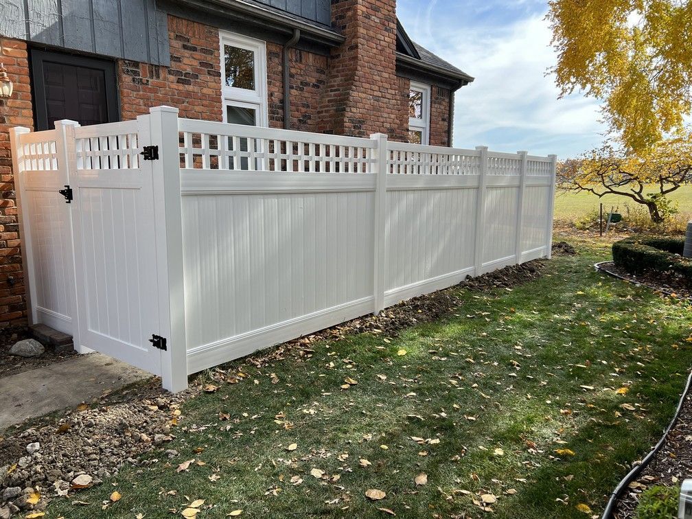 A white vinyl fence is in front of a brick house.