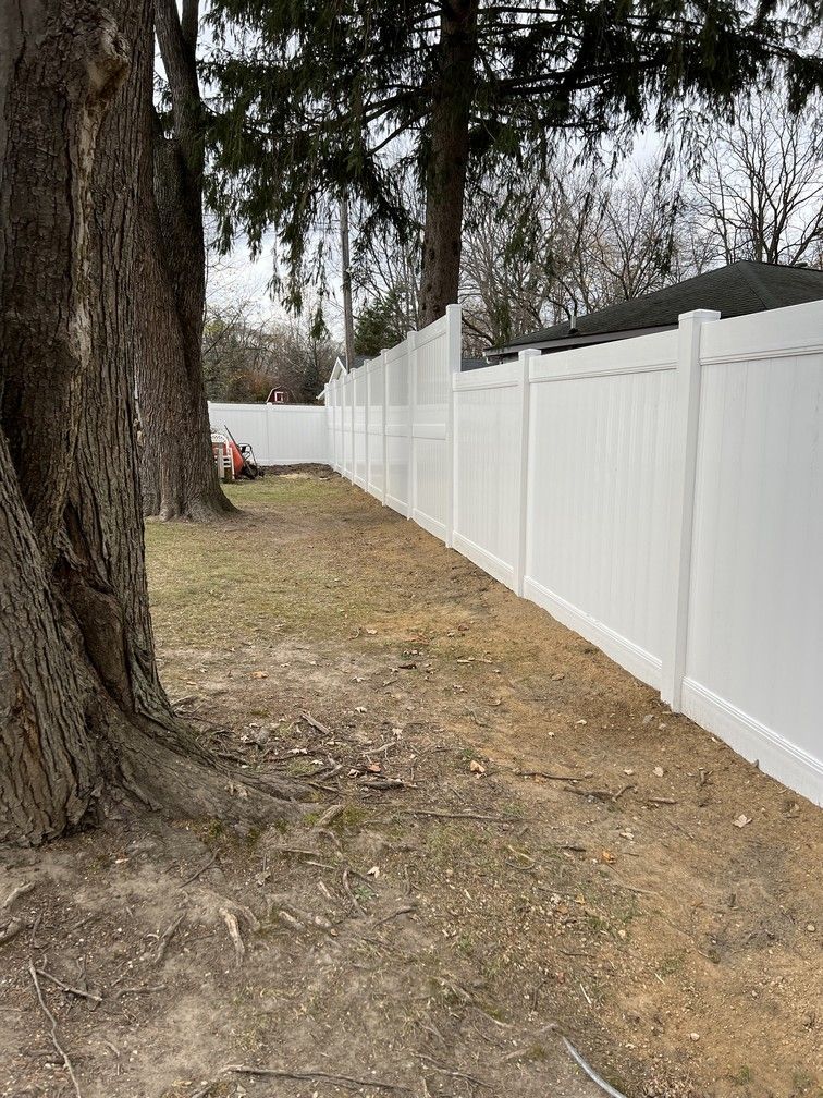 A white fence is surrounded by trees in a yard.