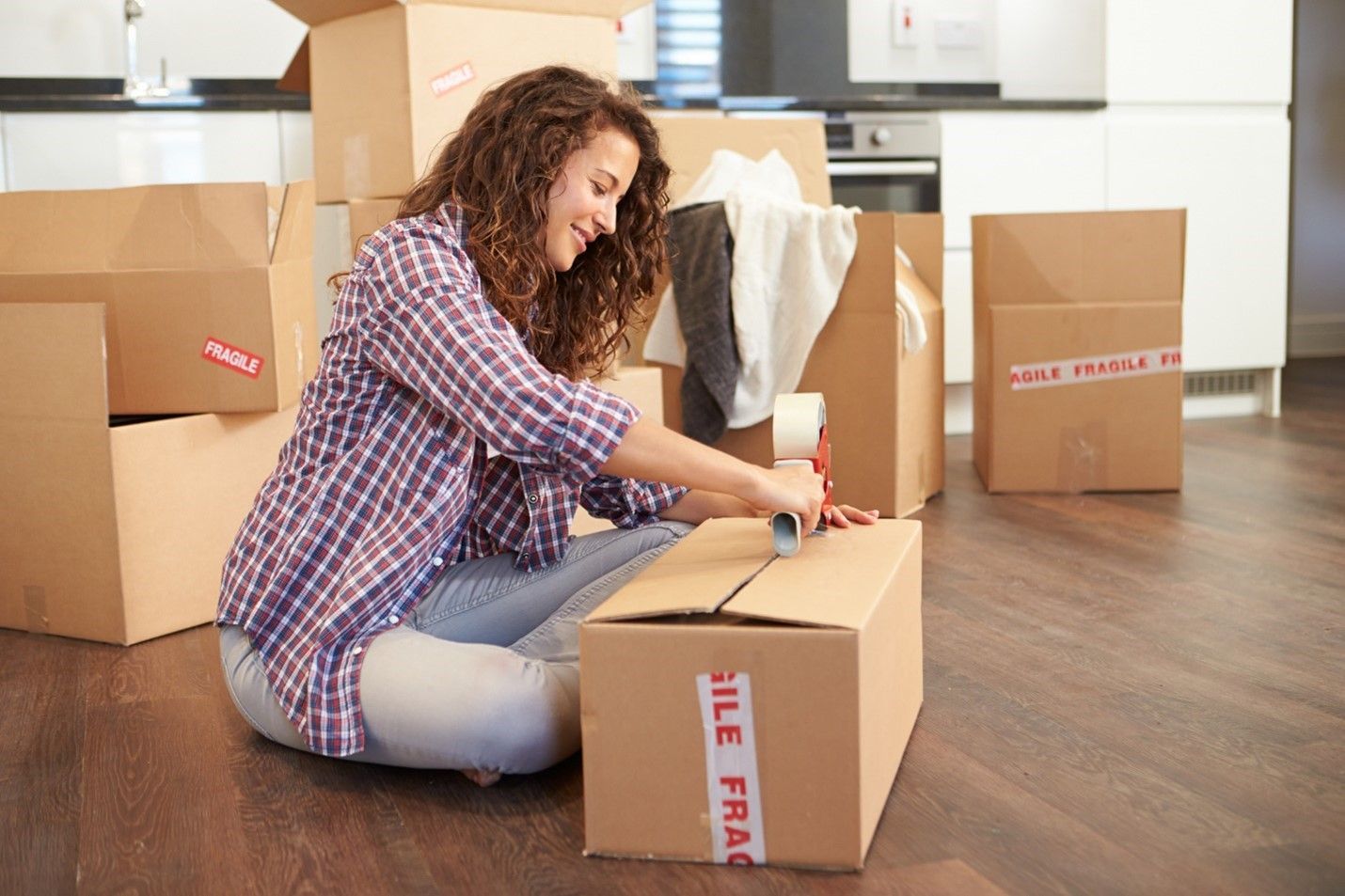 A Woman Is Sitting on The Floor Wrapping a Cardboard Box.