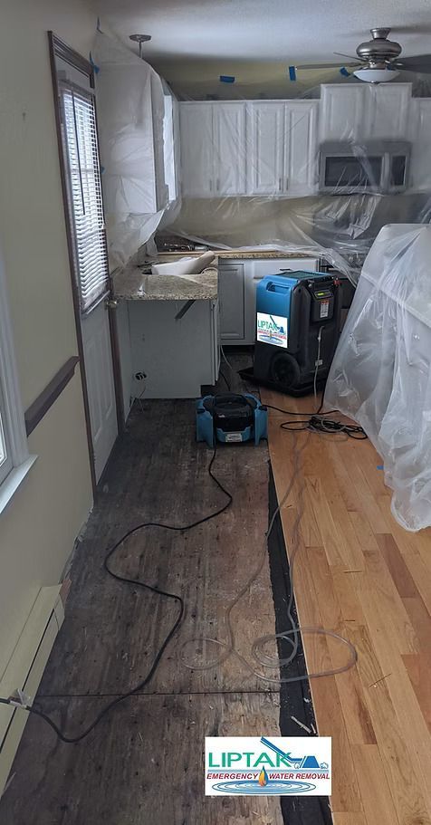 Kitchen renovation in progress: protective coverings, equipment, exposed subfloor, and installed hardwood.