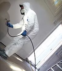 Person in white protective suit spraying a wall with a paint sprayer.