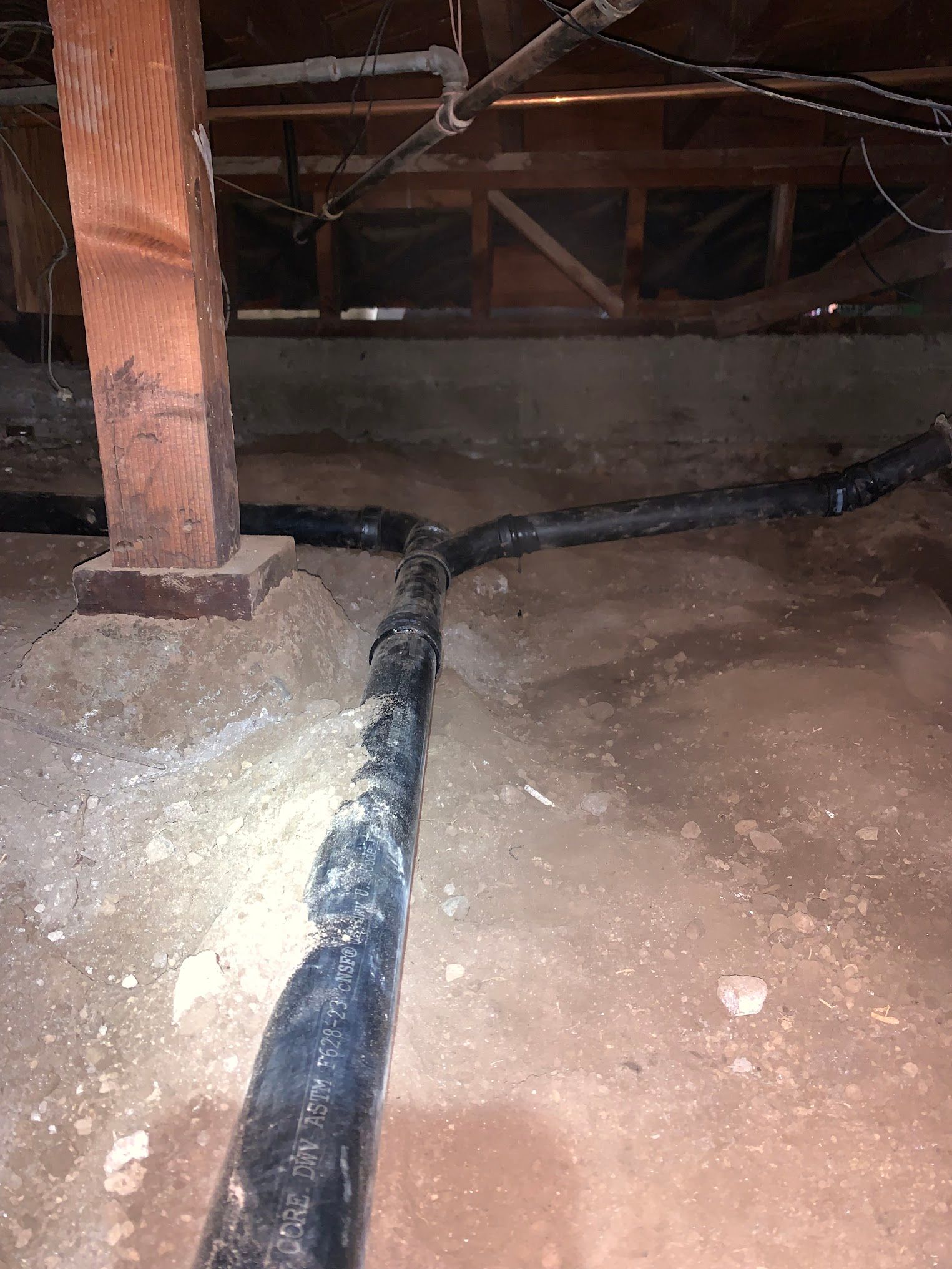 Black plumbing pipes in a crawl space, branching off from a central pipe.
