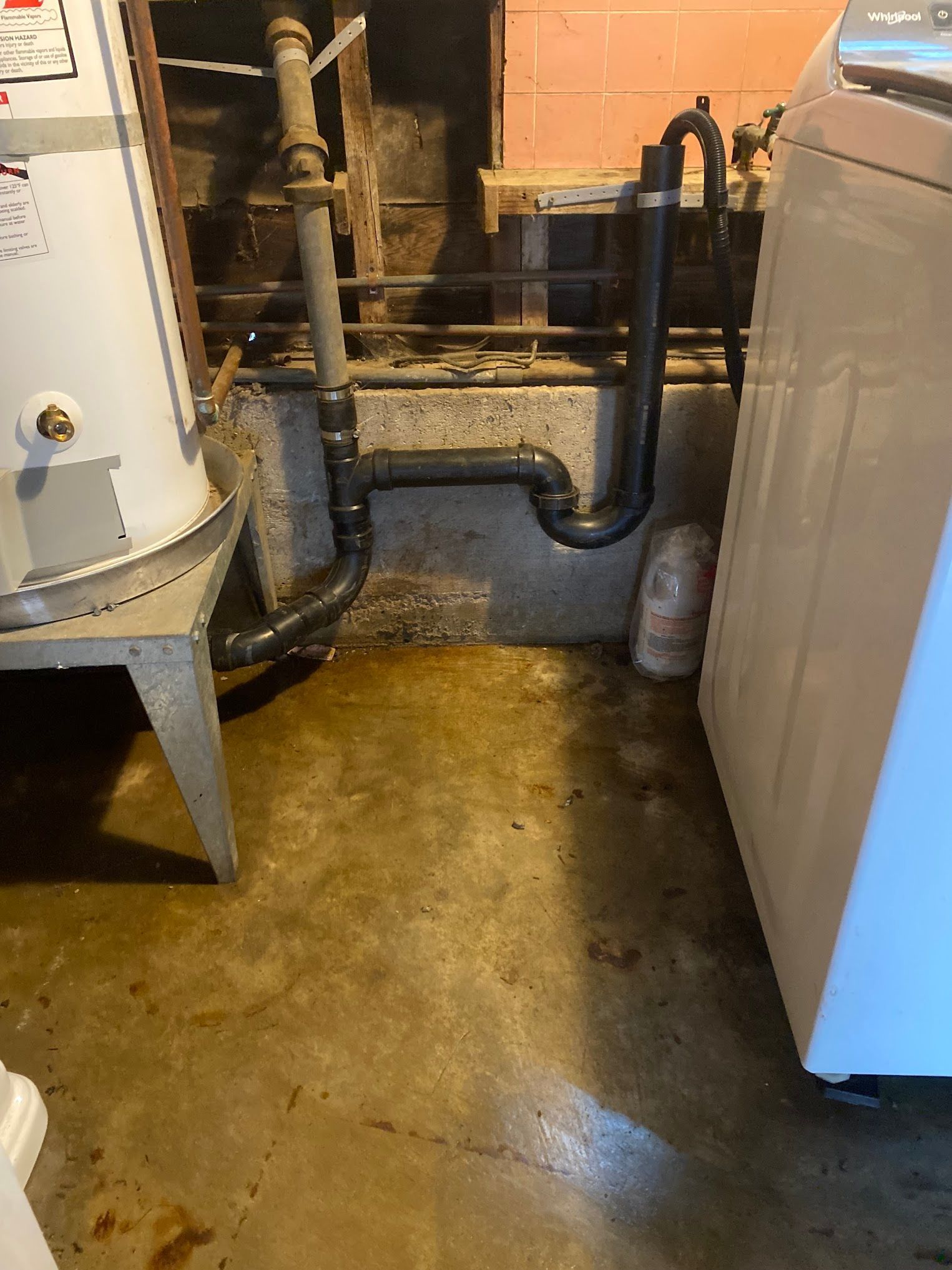 A laundry room with a water heater, washer, and plumbing on a concrete floor.