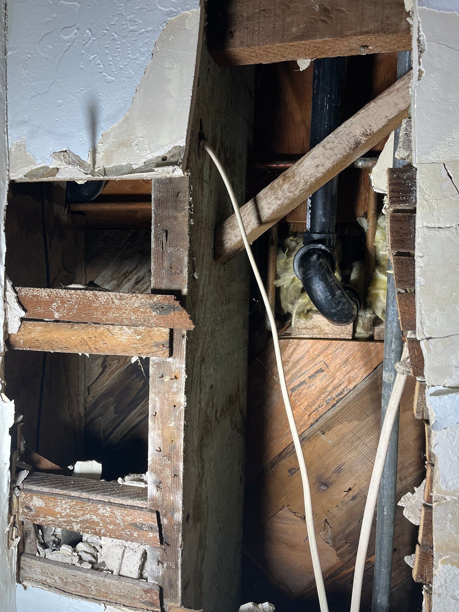 Exposed wall with plumbing pipes and wood beams. Damaged plaster and insulation visible.