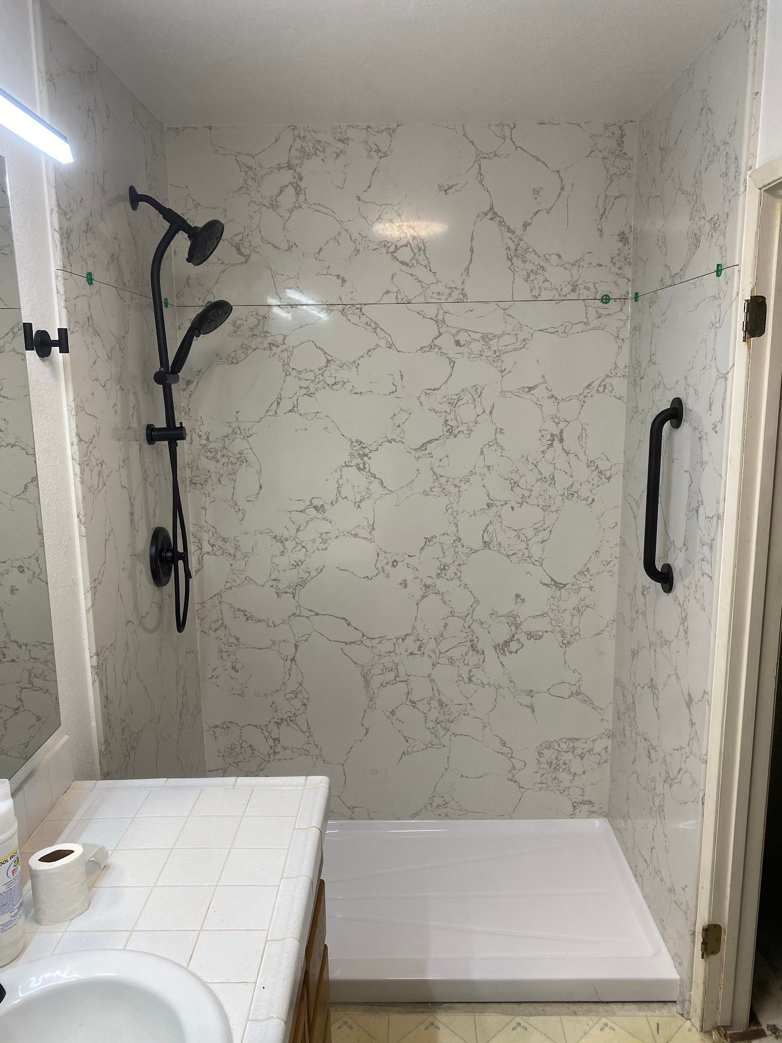 Bathroom with a marble-patterned shower, black fixtures, a grab bar, and a white shower base.