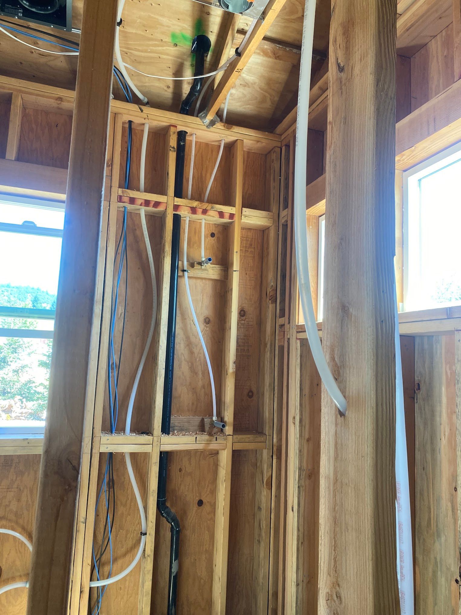 Framed wooden wall with exposed plumbing and wiring, likely during construction.
