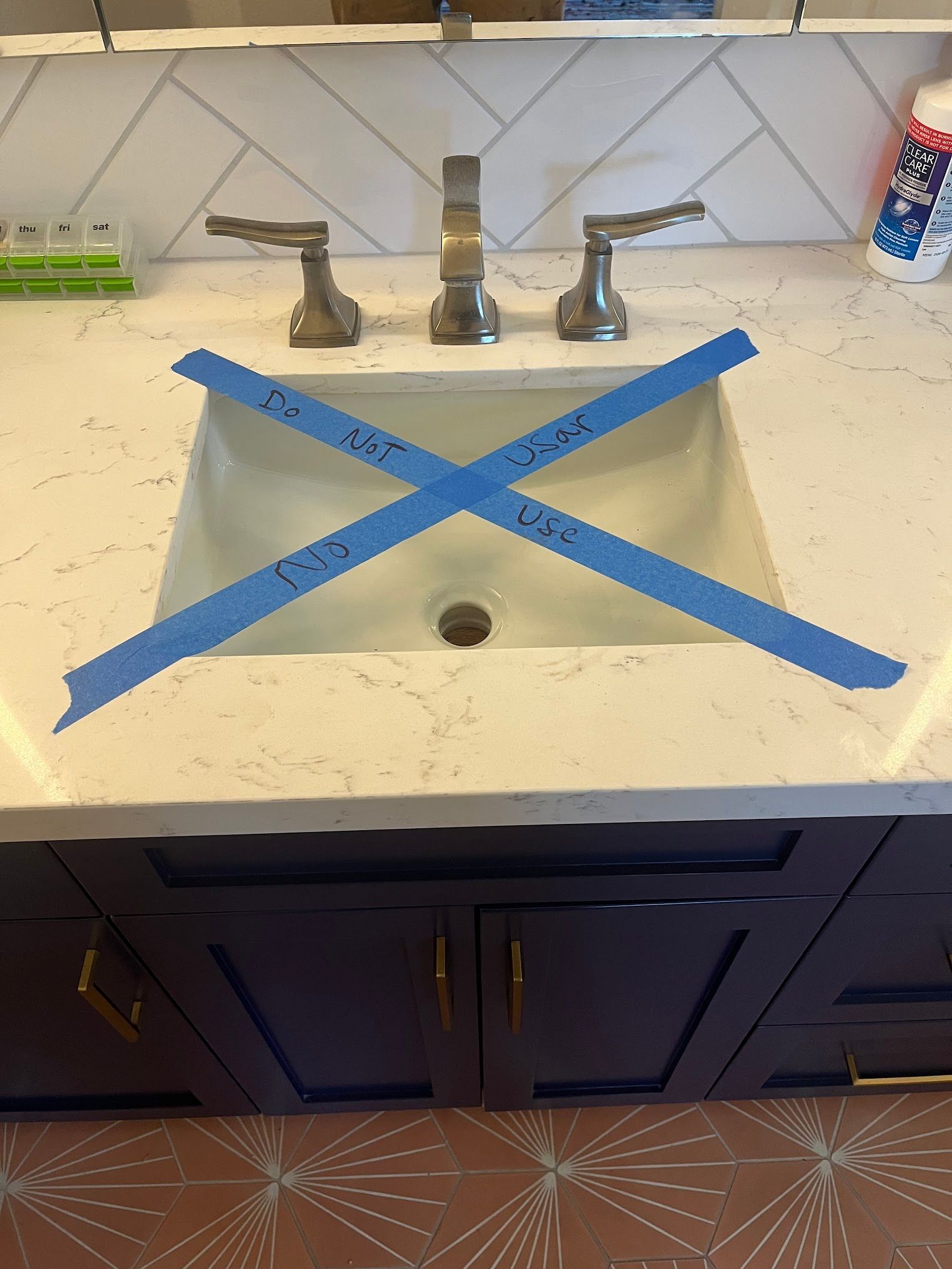 A bathroom sink with blue tape forming an X, indicating it's out of order.