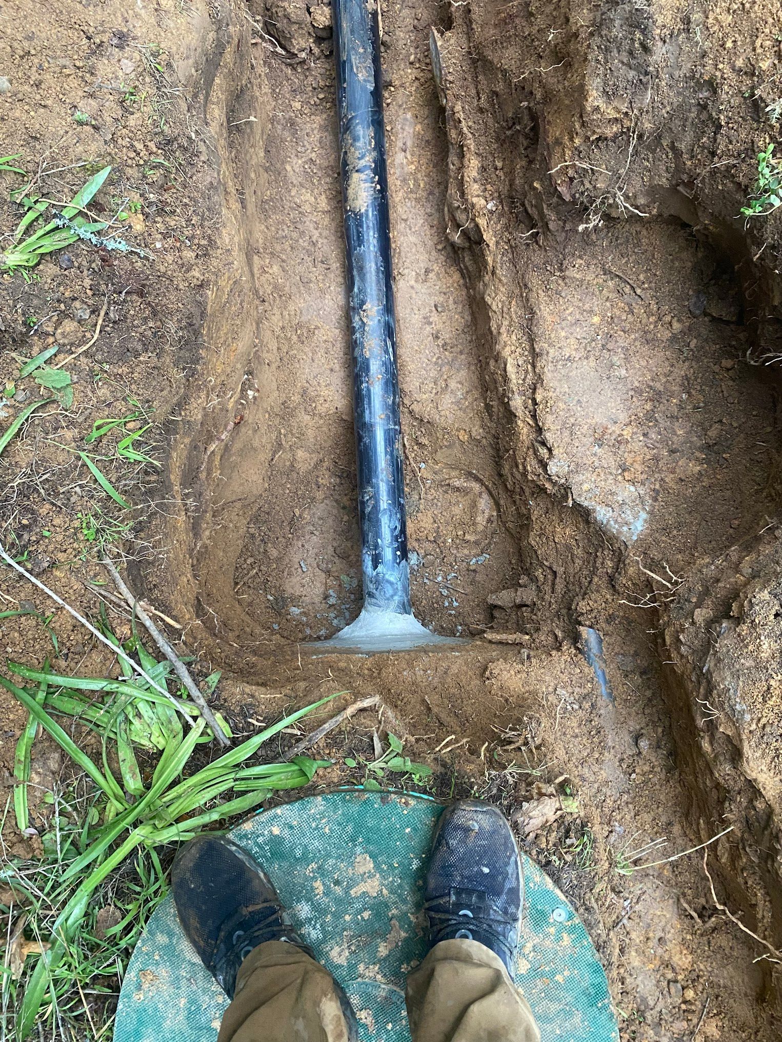 Person standing over a septic tank access point, with a black pipe rising from it.