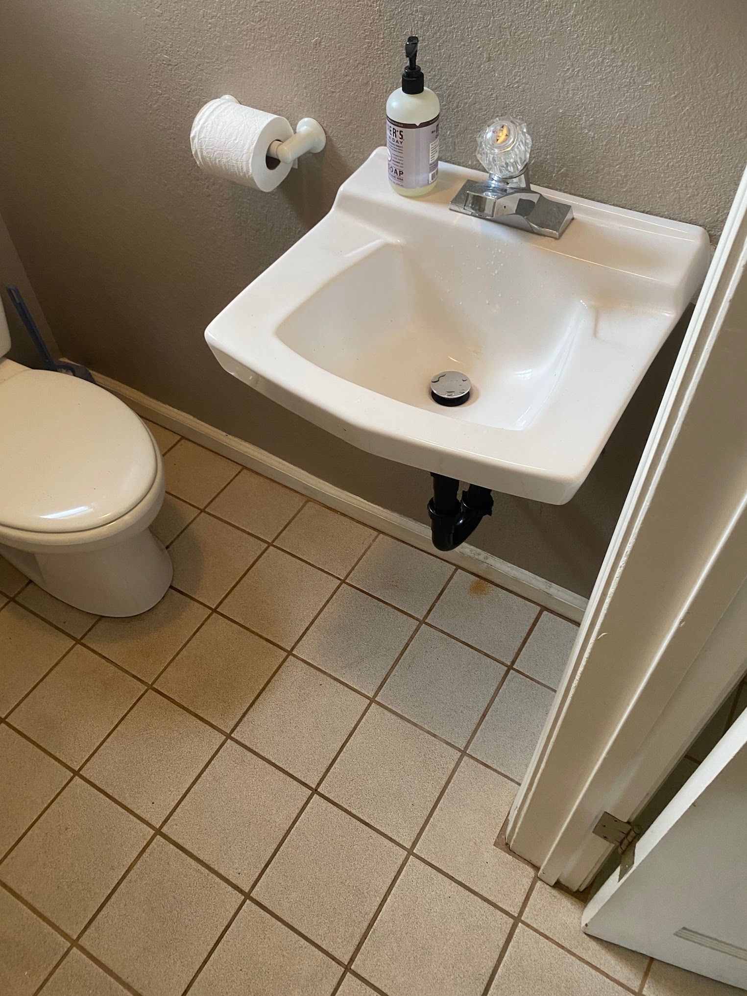 A small white sink and toilet in a bathroom with tan tiled floor and gray walls.