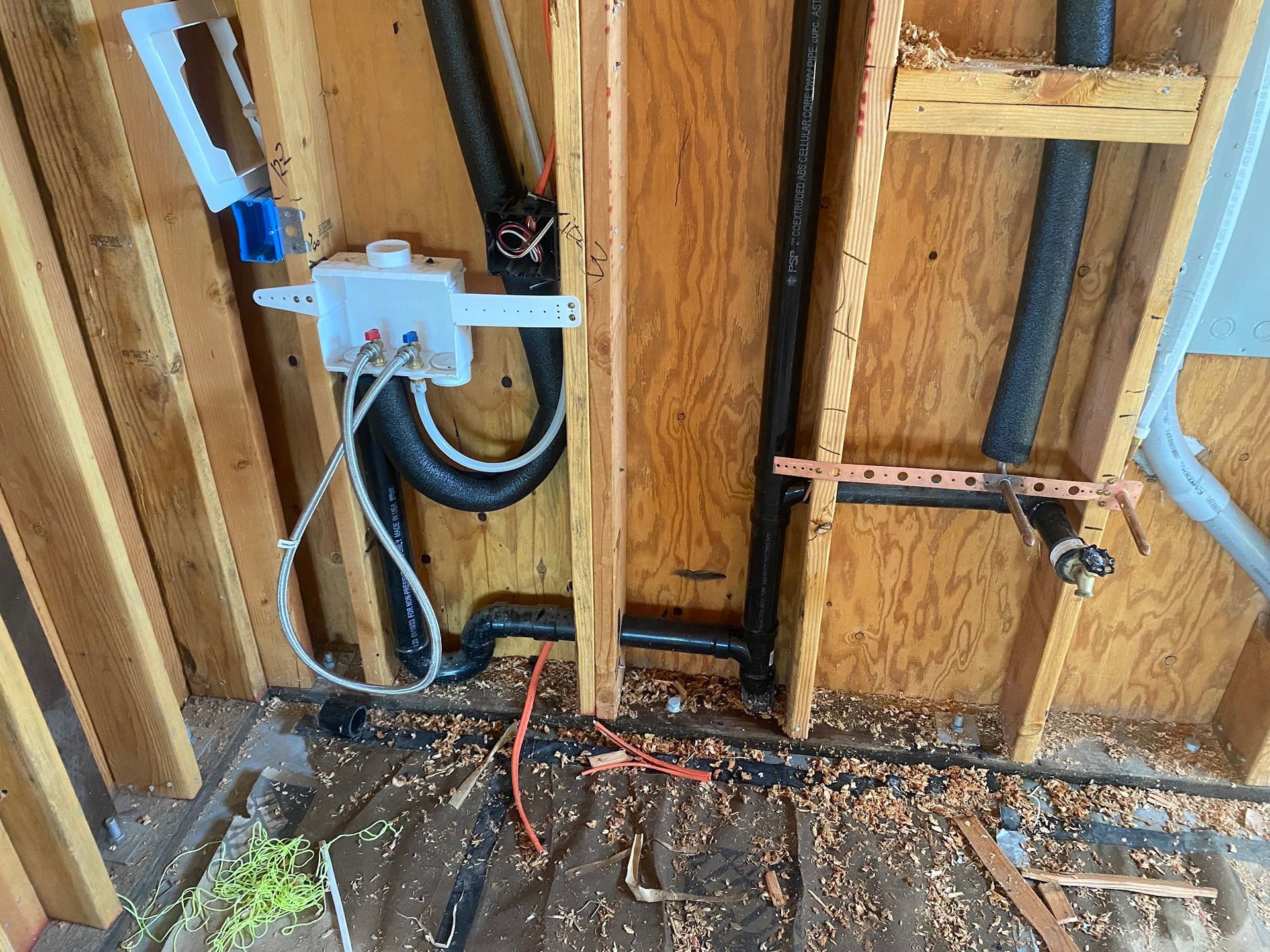 Framing with plumbing, electrical box, and pipes exposed within a wall cavity during construction or renovation.