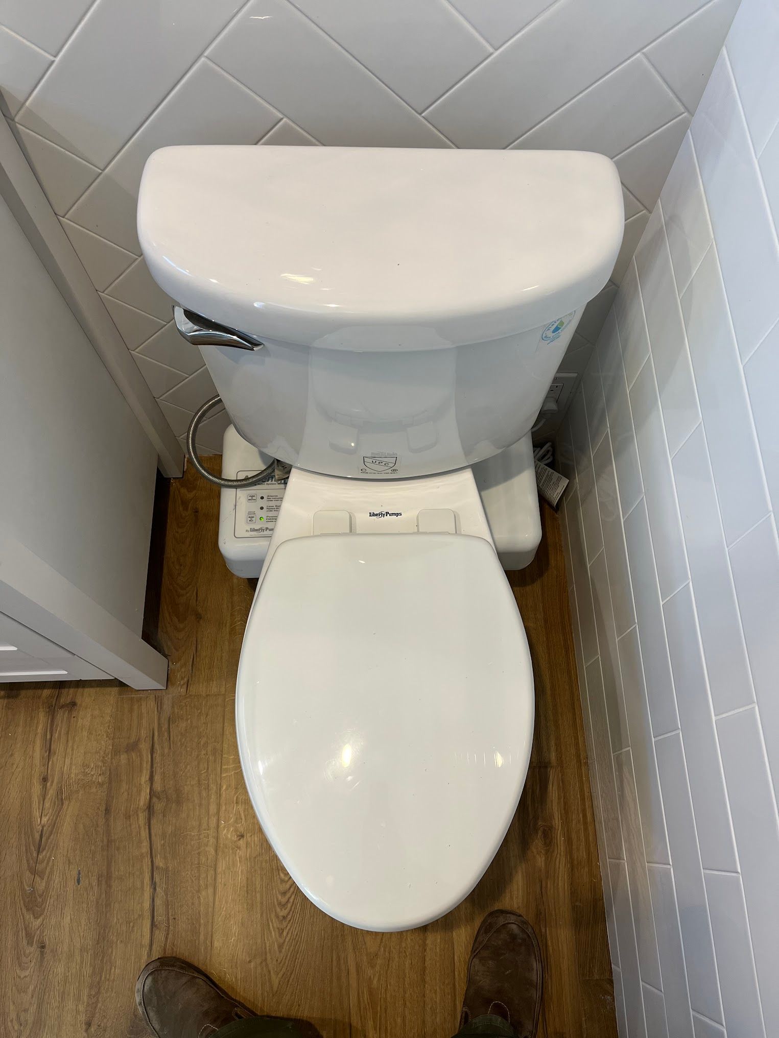 White toilet with a bidet seat, in a small bathroom with wooden floors and white tile walls.